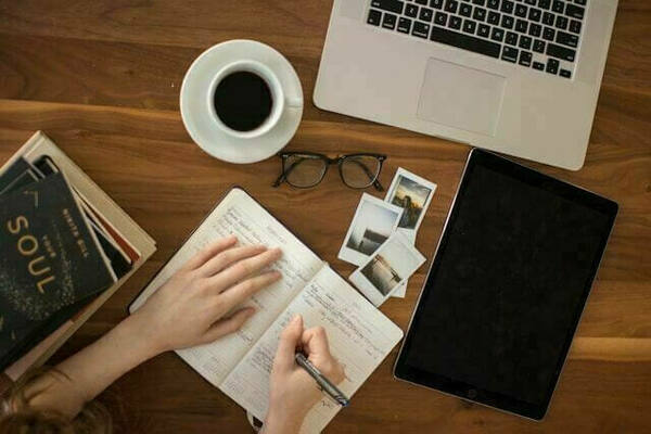 study desk with laptop, coffee cup, notebook and other books on the side